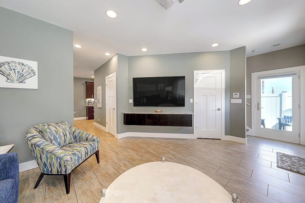 A living room with a flat-screen TV, a patterned armchair, and a round ottoman.