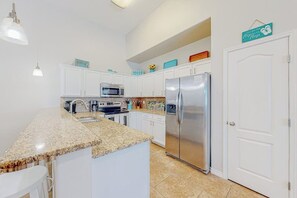 A kitchen with white cabinets, a stainless steel refrigerator, a microwave, and a granite countertop. - Morgan Shores - Pool & Garage, Near the Beach (Port Aransas)