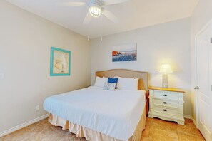 A bedroom with a bed, a nightstand, a ceiling fan, and wall art. - Morgan Shores - Pool & Garage, Near the Beach (Port Aransas)