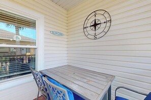 A covered outdoor area with a table and chairs, a compass wall decoration, and a window with blinds. - Palm Bay 304 - Lagoon Pool & Private Patio (Corpus Christi)