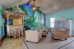 A room with a tropical mural, wicker furniture, a bar area, and a view of the outside. - Palm Bay 304 - Lagoon Pool & Private Patio (Corpus Christi)