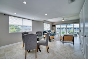 A spacious room with a dining table, chairs, a sofa, and a large window providing a view of a balcony. - Stunning Sunsets & Snorkelling on 7 Mile (George Town)