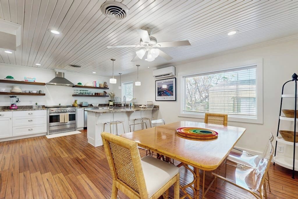 Une cuisine moderne avec un plancher en bois, des meubles blancs, une table à manger avec des chaises et un ventilateur de plafond.
