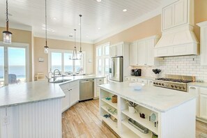 A kitchen with white cabinetry, a central island, a stove, and a view of the ocean. - Reserve at St Charles Bay - Grateful and Gracious (Rockport)