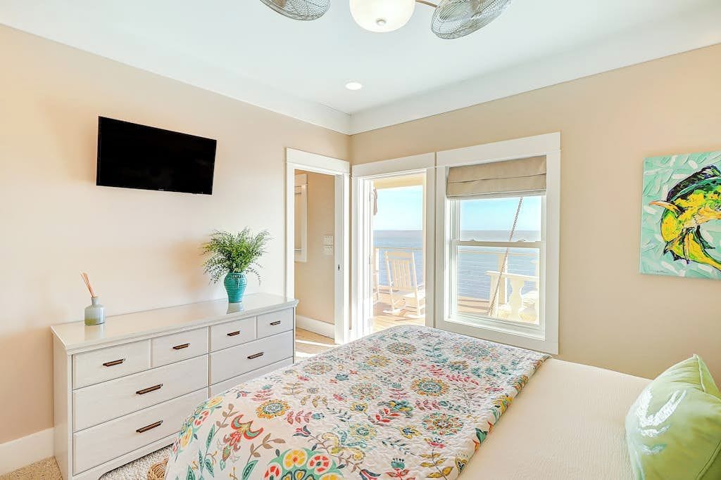 A bedroom with a bed, a dresser, a television, a window with a view, and a door leading to an outdoor area.