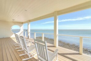 A covered deck with white rocking chairs and a view of the ocean. - Reserve at St Charles Bay - Grateful and Gracious (Rockport)