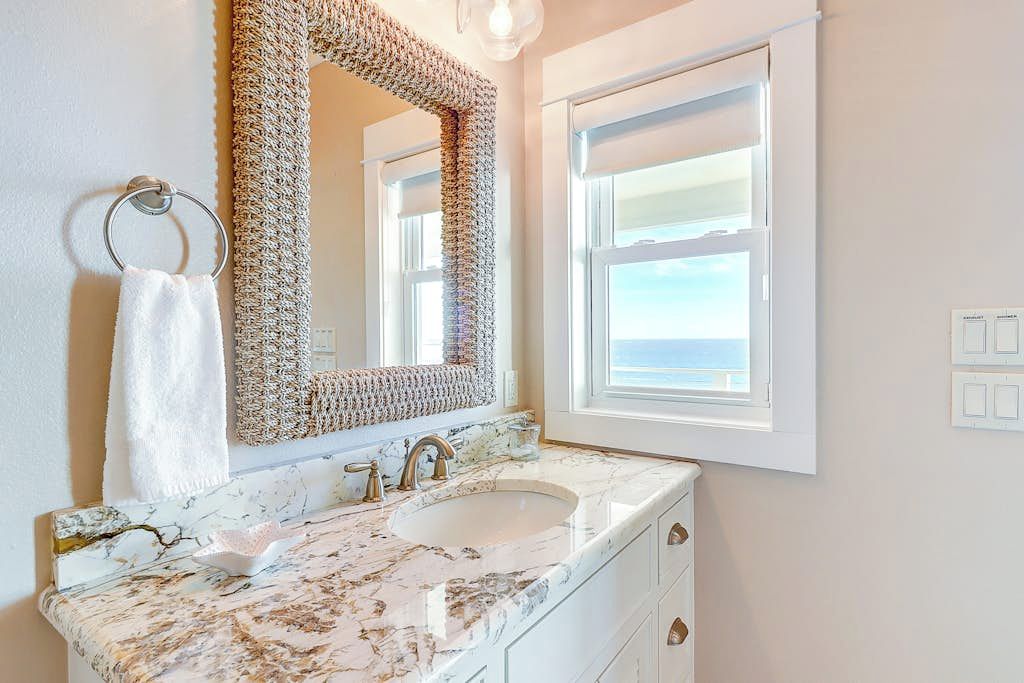 Un bagno con un lavandino in marmo, uno specchio grande e vista mare da una finestra.