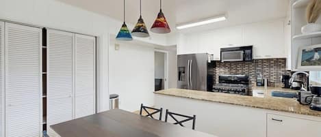 Una cocina moderna con armarios blancos, un refrigerador de acero inoxidable, un microondas y una cafetera.