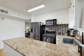 A modern kitchen with white cabinets, stainless steel appliances, and a granite countertop. - The Lazy Oak Retreat (Rockport)