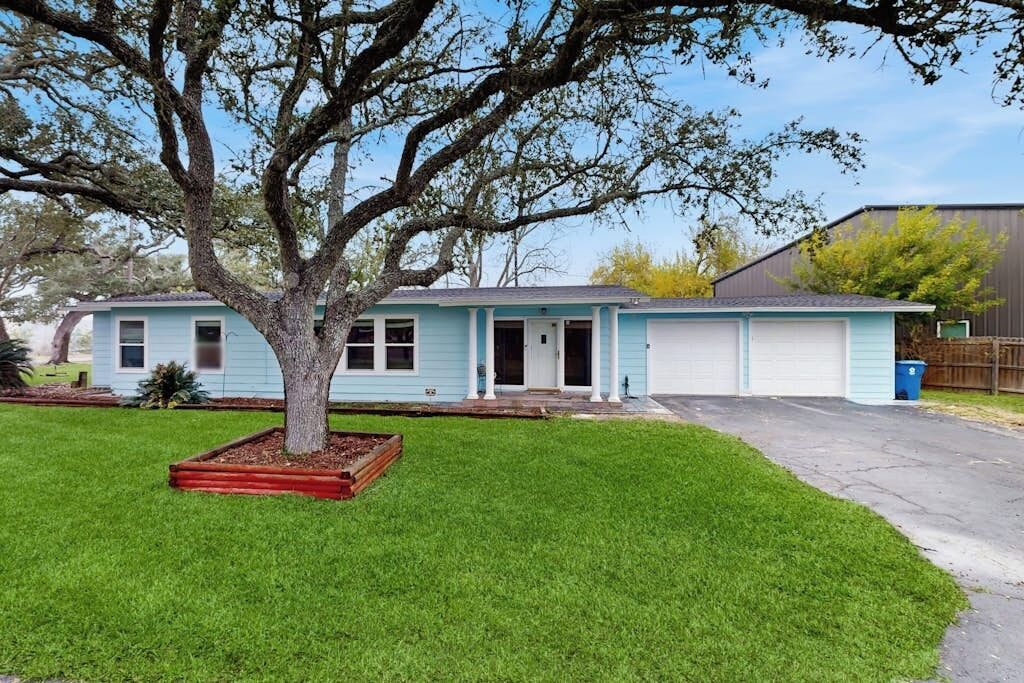 A single-story house with a front garage, a tree in the front yard, and a clear sky.