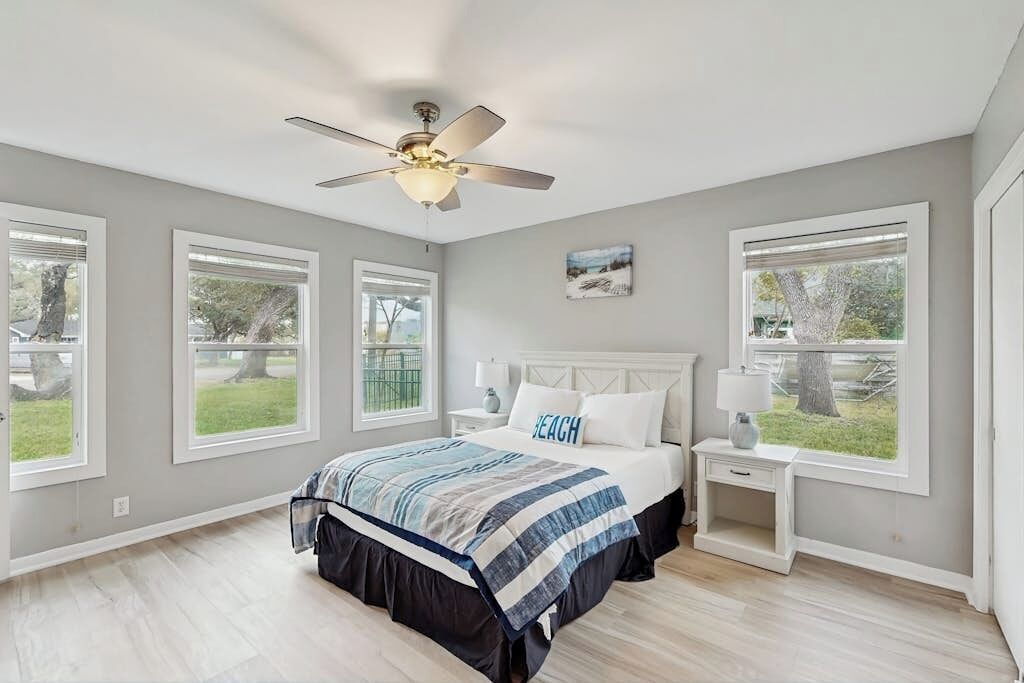 Une chambre à coucher avec un lit, un ventilateur de plafond et de grandes fenêtres.