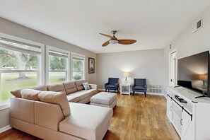 Een woonkamer met een beige modulaire bank, een plafondventilator, een televisie en uitzicht op de omgeving.