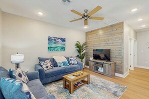 A living room with a sofa, coffee table, TV, and wooden wall paneling. - Rockport Oasis Retreat (Rockport)