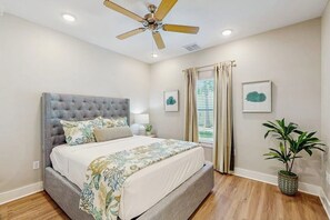 A bedroom with a tufted headboard, a bed with a floral bedspread, a ceiling fan, and a potted plant. - Rockport Oasis Retreat (Rockport)