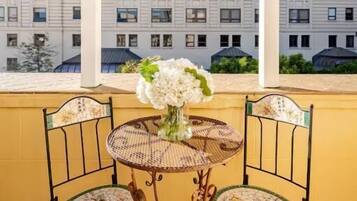 A balcony with a table and chairs, a vase with flowers, and a view of a multi-story building.