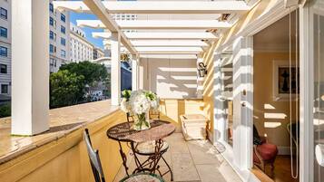 A balcony with a table and chairs, a vase of flowers, and a view of buildings.