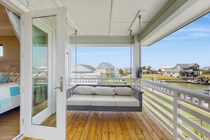 Ein Balkon mit Holzboden, einer weißen gepolsterten Bank und Blick auf Häuser und Wasser.