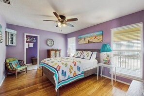 Ein Schlafzimmer mit einem Bett, einem Deckenventilator, einem Fenster mit Jalousien, einem Sessel und einer Wanduhr.