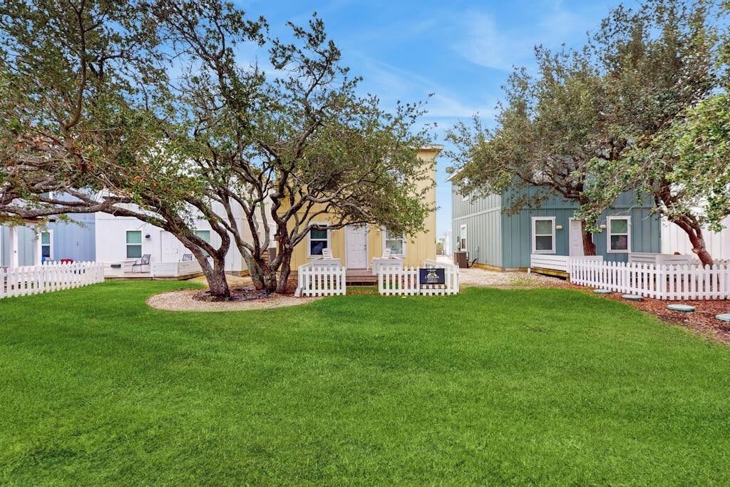 A property with a well-maintained lawn, white picket fence, and a tree in the center.