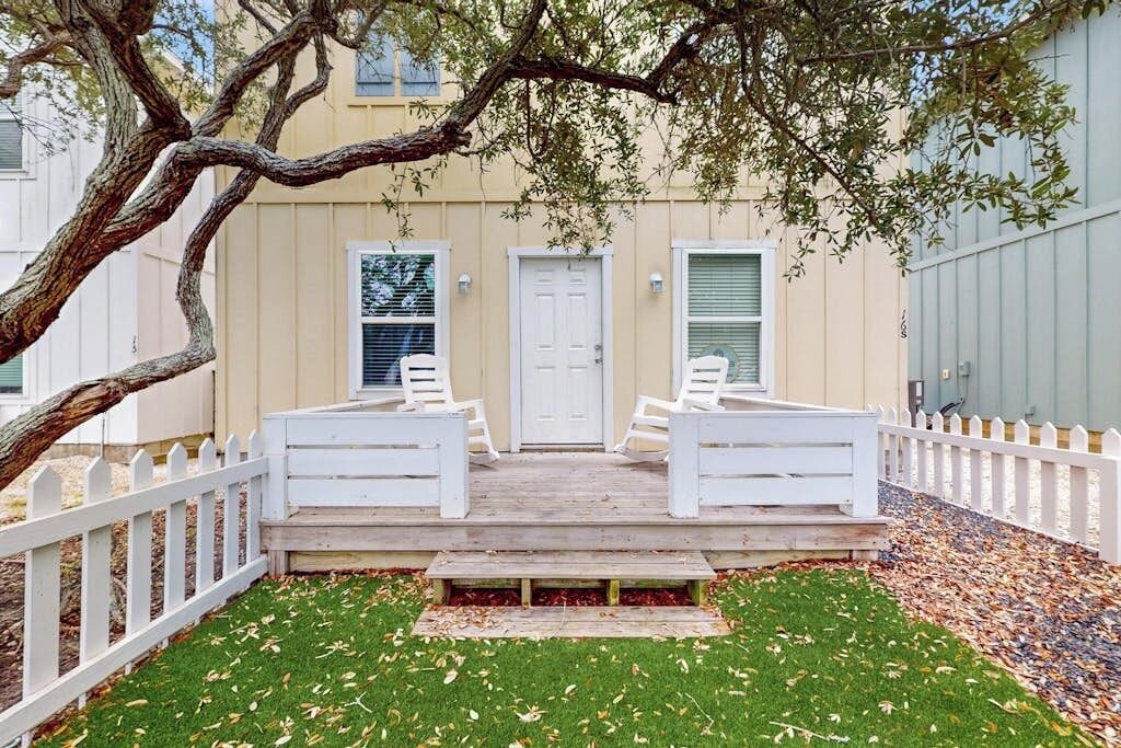 Une maison avec une véranda à l’avant, une clôture en bois peinte en blanc et une pelouse.