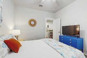 A bedroom with a bed, a television on a dresser, a wall-mounted mirror, and a door leading to a bathroom. - Reel Escape - Pool, Fire Pit & Dog-Friendly (Rockport)