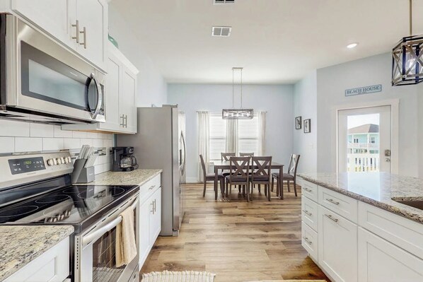A modern kitchen with white cabinets, a microwave, stove, and a dining area with a table and chairs. - Stay Anchored Rockport (Rockport)