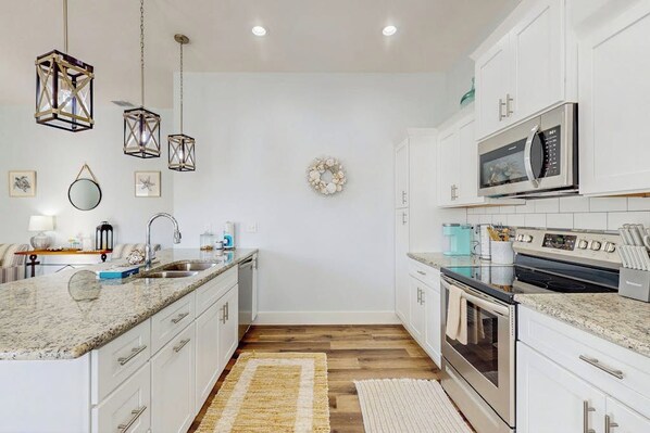 A kitchen with white cabinets, a granite countertop, a stainless steel oven, and a microwave. - Stay Anchored Rockport (Rockport)
