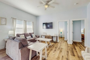 A living room with a sofa, coffee table, and TV. There are wooden floors and a ceiling fan. - Stay Anchored Rockport (Rockport)