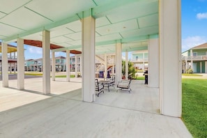 A covered outdoor area with a concrete floor, white pillars, and metal furniture. - Stay Anchored Rockport (Rockport)