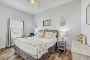 A bedroom with a bed, bedside tables, a nightstand, a ceiling fan, and a window with curtains. - Stay Anchored Rockport (Rockport)