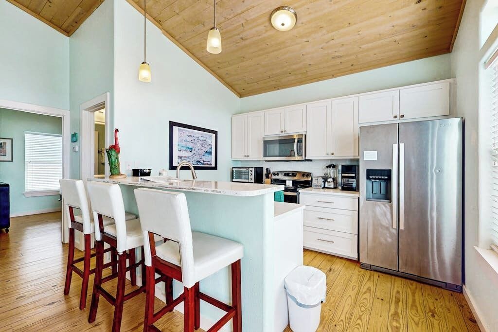 A modern kitchen with white cabinets, stainless steel appliances, and a wooden ceiling.