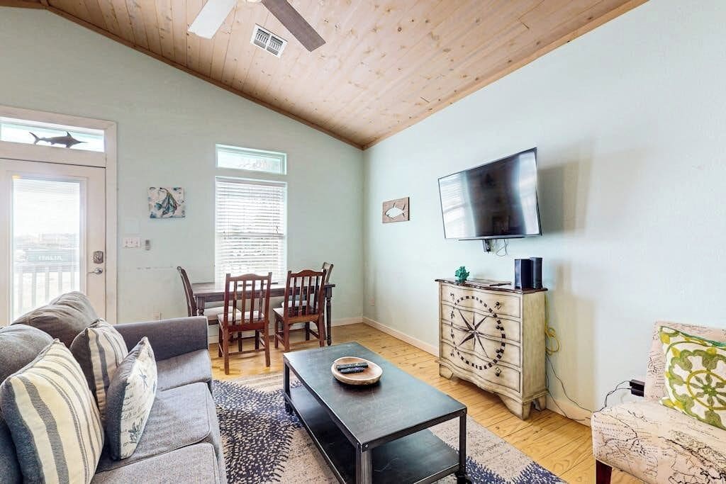 A living room with a sofa, a coffee table, a TV, a wooden cabinet, and a dining area with chairs.