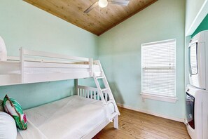A bunk bed room with a ceiling fan, a window with blinds, and a kitchenette area. - Eskridge Gem - Both Homes (Port Aransas)