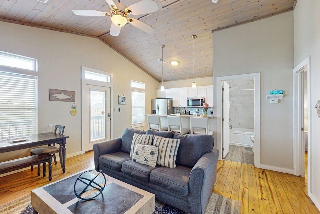 A spacious living area with a gray sofa, wooden dining table, and a ceiling fan.