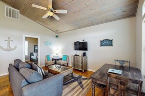 A living room with a ceiling fan, a TV, a dining table, and a sofa. - Eskridge Gem - Both Homes (Port Aransas)