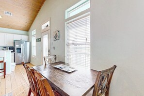A kitchen with wooden cabinets, a stainless steel refrigerator, and a dining table with chairs. - Eskridge Gem - Both Homes (Port Aransas)