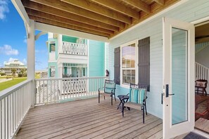 A wooden porch with a white railing, a bench, and a door leading to an interior space. - The Conch Casa - Steps to the Beach, Sleeps 9 (Galveston)
