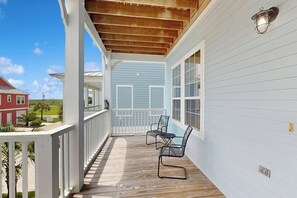 Varanda coberta com deck de madeira, grades brancas e vista para casas vizinhas.