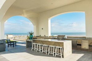 An outdoor kitchen area with a bar stool seating arrangement, overlooking a beach. - Emerald By The Sea #603 (Galveston)