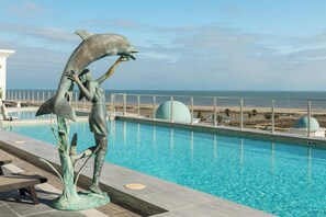 A swimming pool with a dolphin statue and a view of the ocean. - Emerald By The Sea #603 (Galveston)