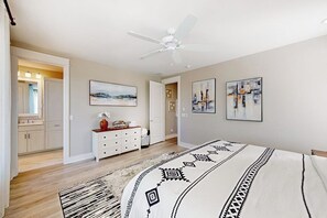 A bedroom with a bed, a ceiling fan, a dresser, and artwork on the walls.