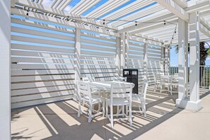 Un espacio de estar al aire libre techado, con mobiliario blanco y una estructura de pérgola.