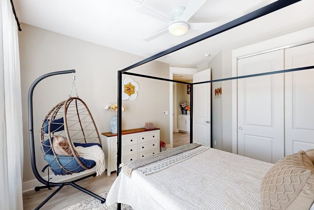 A bedroom with a four-poster bed, a hanging chair, a dresser, and a door leading to another room.