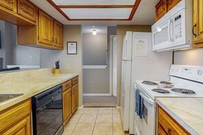 A compact kitchen with wooden cabinets, a dishwasher, a microwave, and a stove. - Seagull Cove - Waterfront, Bay Views & Garage (Galveston)