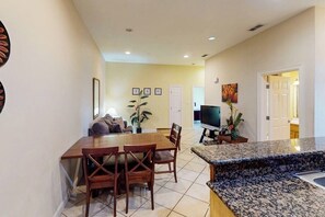 A dining area with a wooden table and chairs, a TV, and a kitchen counter. - Shoreline Oasis - Shared Pool, Steps to the Beach (South Padre Island)