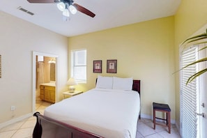 A bedroom with a bed, a nightstand, a ceiling fan, and a door with blinds. - Shoreline Oasis - Shared Pool, Steps to the Beach (South Padre Island)