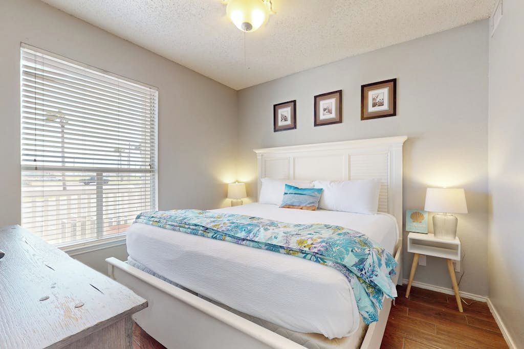 Une chambre à coucher avec un lit, des tables de chevet, une fenêtre avec des stores et des tableaux accrochés au mur.
