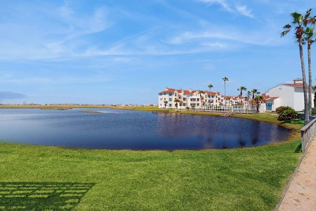 A hotel with a large body of water in front, a well-maintained lawn, and a clear sky.