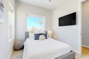 A bedroom with a bed, a television mounted on the wall, a window, and a door. - Dolphin Paradise Unit A (South Padre Island)