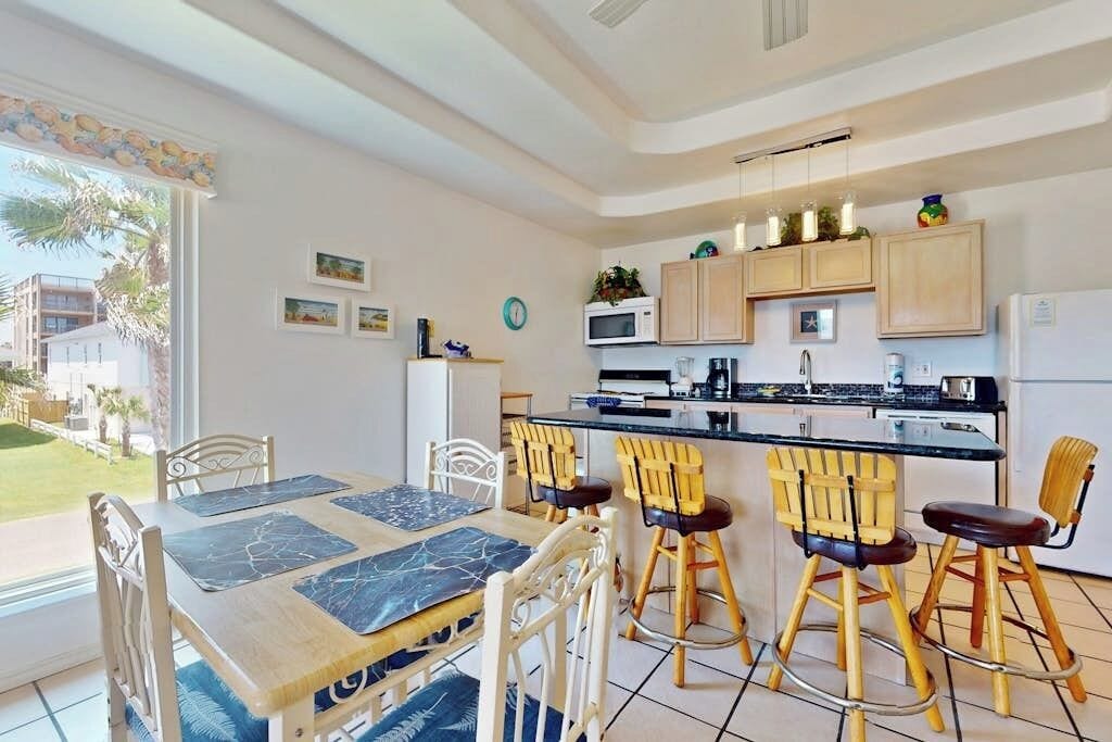 A modern kitchen with a dining area, featuring a large island with bar stools, a refrigerator, and a microwave.